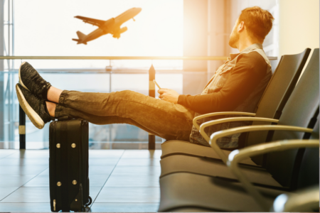 Man sitting on a chair, resting his feet on a suitcase while watching a plane take-off